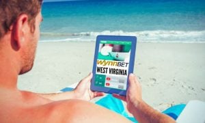 Man Plays Online Casino With Tablet On the Beach with WynnBET West Virginia logo