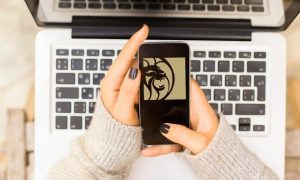 hands holding cell phone bearing betmgm logo over computer