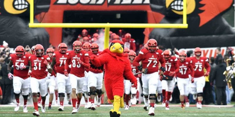university of louisville american football players and mascot run onto a field