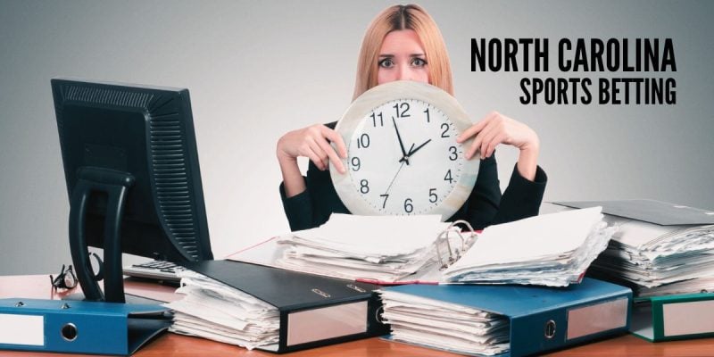 Woman Holds Clock At Cluttered Work Desk with North Carolina sports betting
