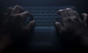 Hacker hands on laptop keyboard, shadowy lighting
