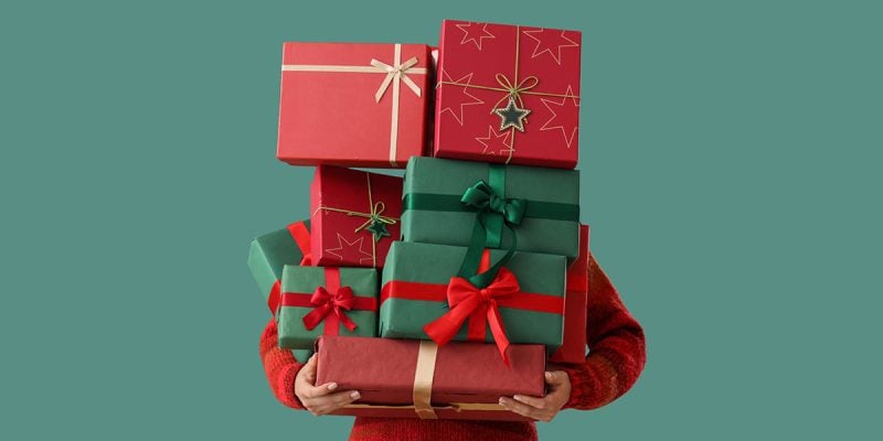 person with arms full of christmas gifts on a green background