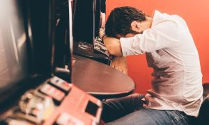 a man puts his head down on a slot machine
