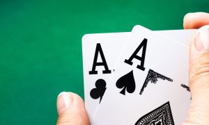 a pair of aces being held over a poker table