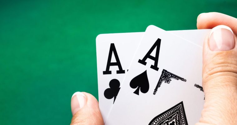 a pair of aces being held over a poker table