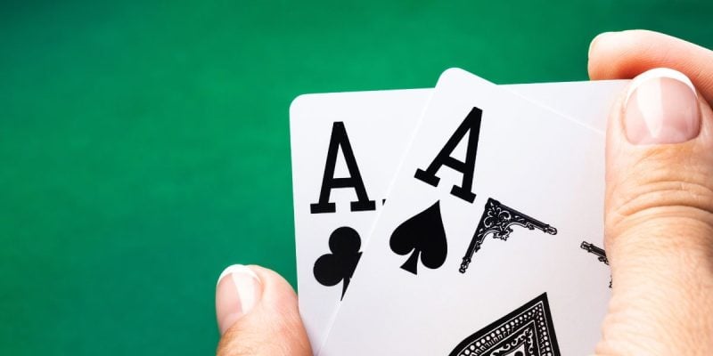 a pair of aces being held over a poker table