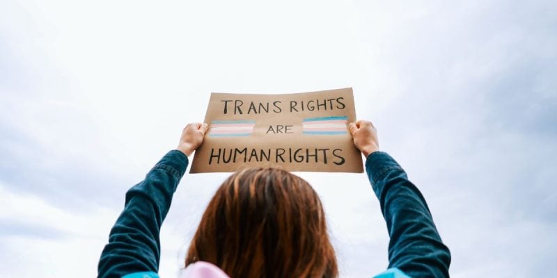 a woman holding up a sign that says trans rights are human rights