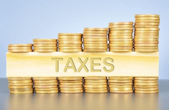stacks of gold coins with a gold bar reading taxes in the middle