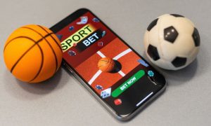 a mobile phone with sports betting on it next to a mini basketball and mini soccer ball