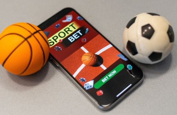 a mobile phone with sports betting on it next to a mini basketball and mini soccer ball