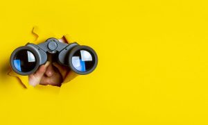 a person peering through a yellow background with binoculars