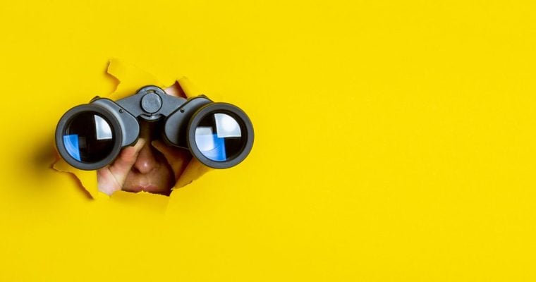 a person peering through a yellow background with binoculars