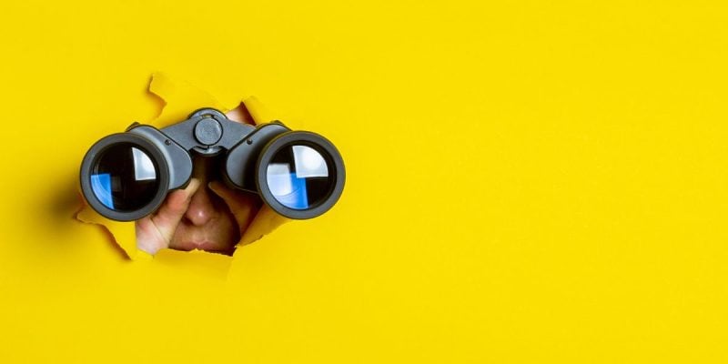a person peering through a yellow background with binoculars