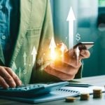 Man Types On Calculator while Holding Mobile Phone