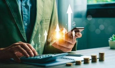 Man Types On Calculator while Holding Mobile Phone