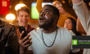 Enthused Black Man Watching Holding Mobile Phone with DraftKings Logo