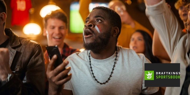 Enthused Black Man Watching Holding Mobile Phone with DraftKings Logo