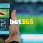 Bet365 logo Centered Over Man Holding Cell Phone and Watching Game on TV