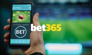 Bet365 logo Centered Over Man Holding Cell Phone and Watching Game on TV