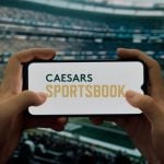 Hands Hold Cell Phone with Caesars Sportsbook Logo inside Football Stadium