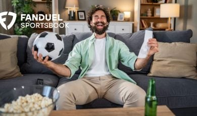 Man Holding Soccer Ball Sits On Couch, Happy About Game Win with FanDuel Logo