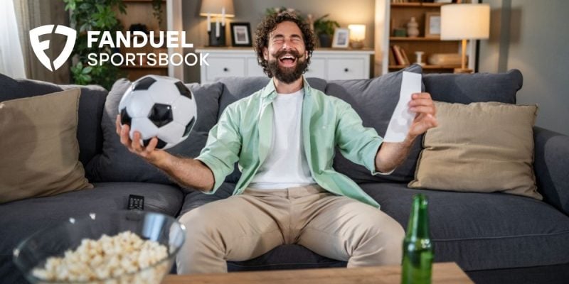 Man Holding Soccer Ball Sits On Couch, Happy About Game Win with FanDuel Logo