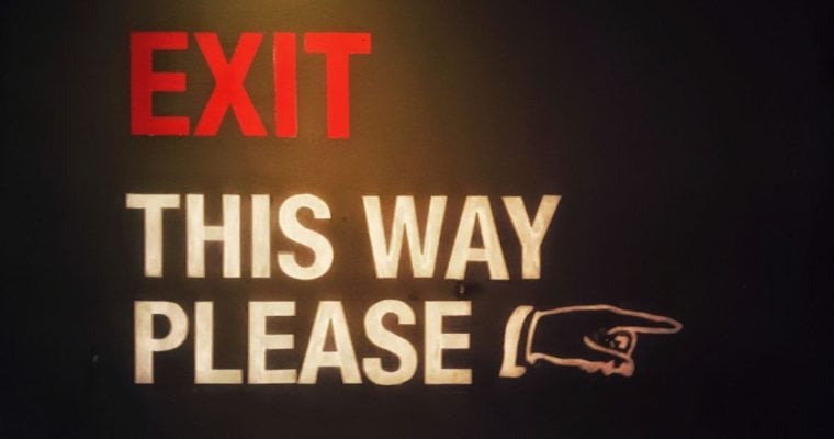 Red and White Exit Sign Reads "Exit This Way Please" With Hand Pointing