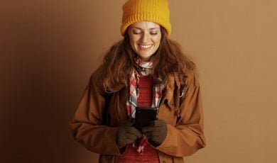 Woman Dressed in Autumn Clothes Holding Cell Phone Smiles