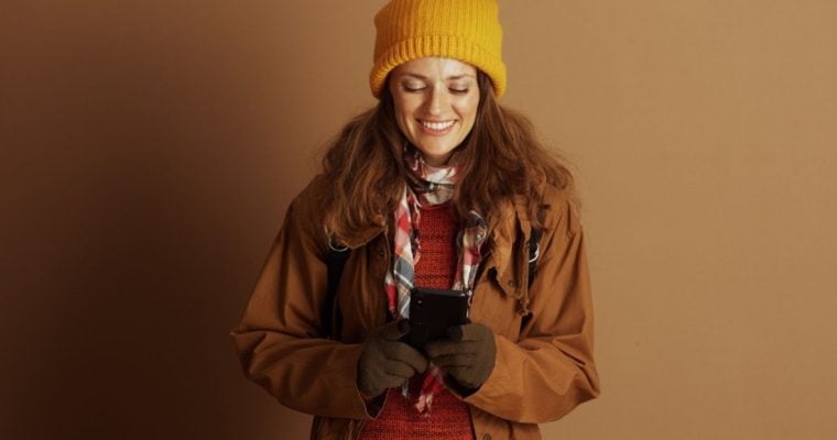 Woman Dressed in Autumn Clothes Holding Cell Phone Smiles