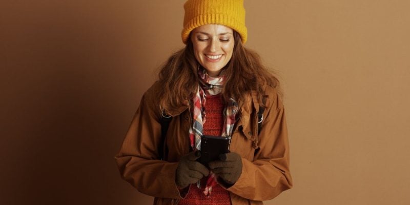 Woman Dressed in Autumn Clothes Holding Cell Phone Smiles