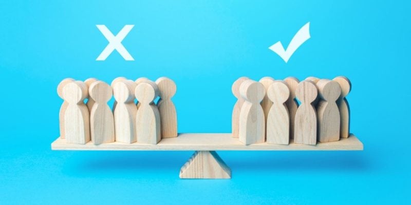 Various People-Shaped Wood Figures Balance On A Scale