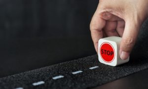 Man Holds Small Wood Block Reading "Stop" on Dashed Line Street