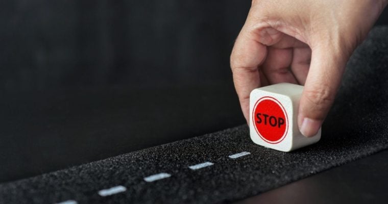 Man Holds Small Wood Block Reading "Stop" on Dashed Line Street