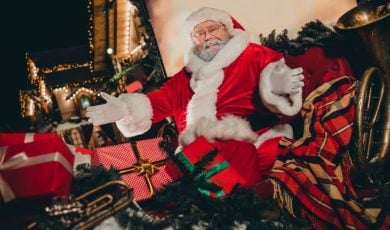 Open-Armed Santa Sits On Christmas Sleigh Full of Wrapped Gifts