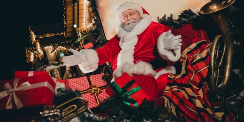 Open-Armed Santa Sits On Christmas Sleigh Full of Wrapped Gifts