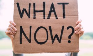 Cardboard Sign Reads "What Now?" In Black