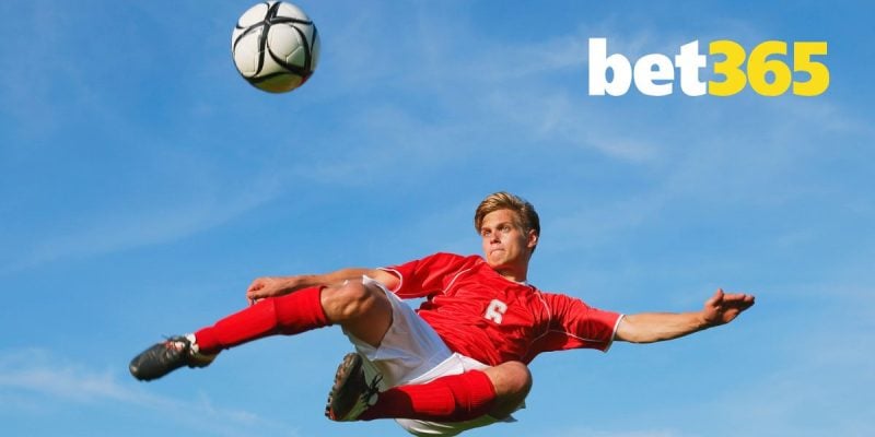 Bet365 Logo Over Image of Soccer Player Mid-Air Kicking Ball Against Blue Sky Background