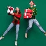 Man and Woman Jumping with Wrapped Gifts Wearing Festive Christmas Outfits