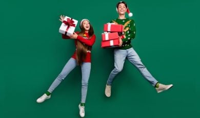 Man and Woman Jumping with Wrapped Gifts Wearing Festive Christmas Outfits