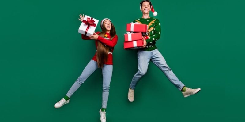 Man and Woman Jumping with Wrapped Gifts Wearing Festive Christmas Outfits