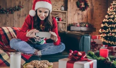 Woman Plays On Cell Phone While Sitting on Couch In Santa Hat