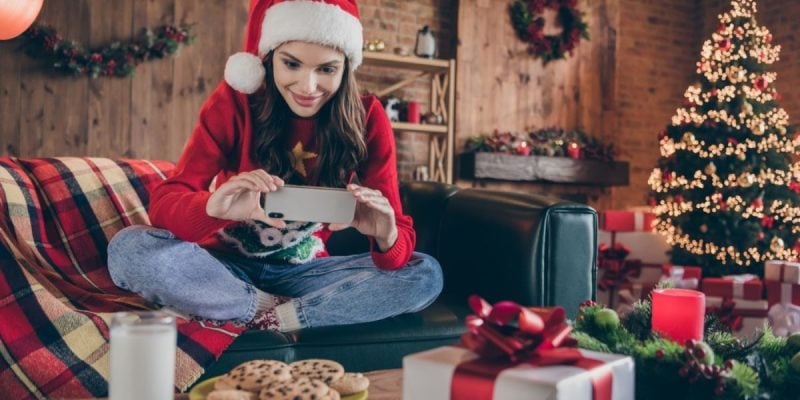 Woman Plays On Cell Phone While Sitting on Couch In Santa Hat