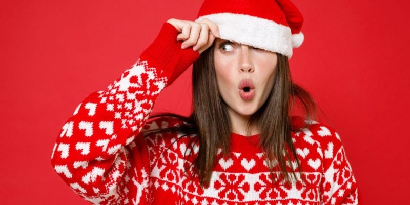 Woman With Surprised Look Wears Santa Hat And Christmas Sweater