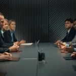 Inside A Dark Office Group of Business Men and Women Sit Across from Each Other