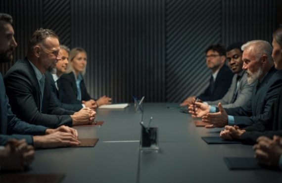 Inside A Dark Office Group of Business Men and Women Sit Across from Each Other