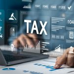 Man Points to Graph On Paper Sits In Front of Laptop with 