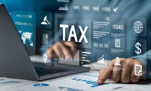 Man Points to Graph On Paper Sits In Front of Laptop with "Tax" Digital Graphics Overlay