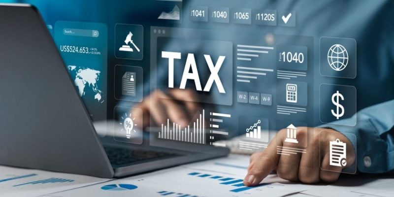 Man Points to Graph On Paper Sits In Front of Laptop with 