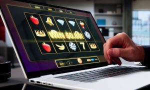 Online Slot Game Displayed on Laptop with Man's Hand Over Keyboard