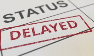 Close Up of White Document Reading Status Delayed in Black and Red Letters